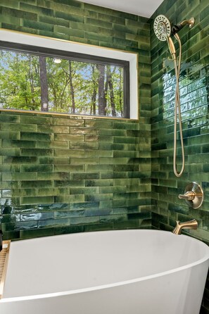 Un bagno con una vasca freestanding, una doccia con soffione manuale e una finestra vista alberi.