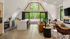 Una cocina moderna con una isla central, una zona de comedor con sofá y sillas, y una sala de estar con chimenea.