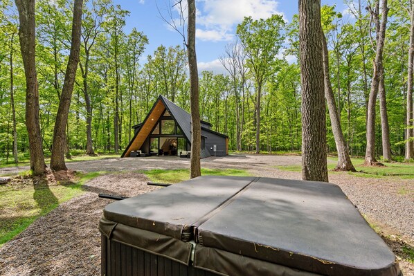 A cabin in a forest with a large deck and a covered outdoor seating area.