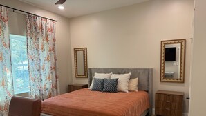 Quarto com cama, mesa de cabeceira, penteadeira, cadeira e janela com cortinas.