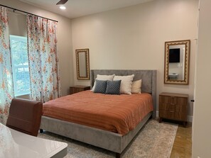 A bedroom with a bed, a nightstand, a dresser, a chair, and a window with curtains.