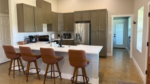 Cozinha moderna com ilha central, banquetas, eletrodomésticos de aço inoxidável e armários em tons claros.