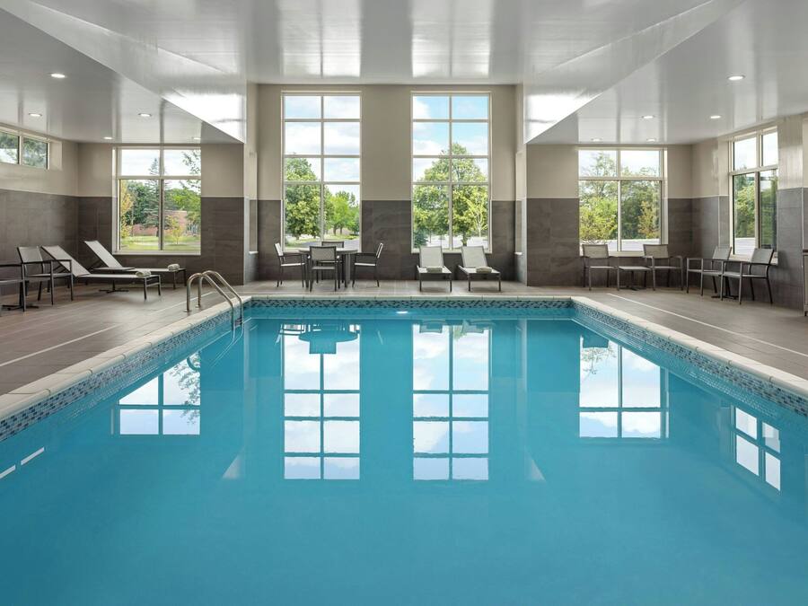 Ein Swimmingpool mit Liegestühlen und Blick auf Bäume durch große Fenster.