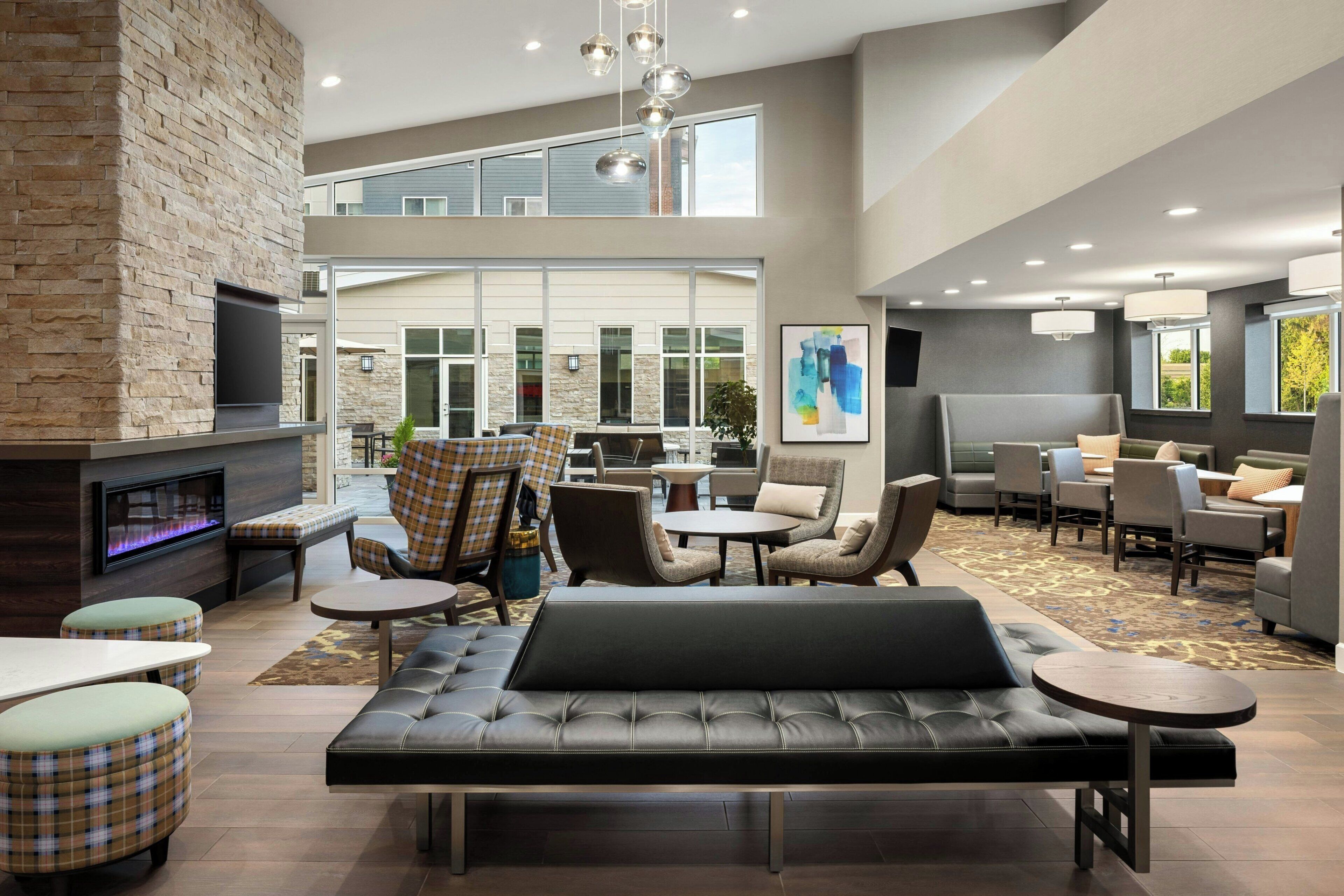 A spacious lobby with a fireplace, seating areas, and a large window overlooking a building.