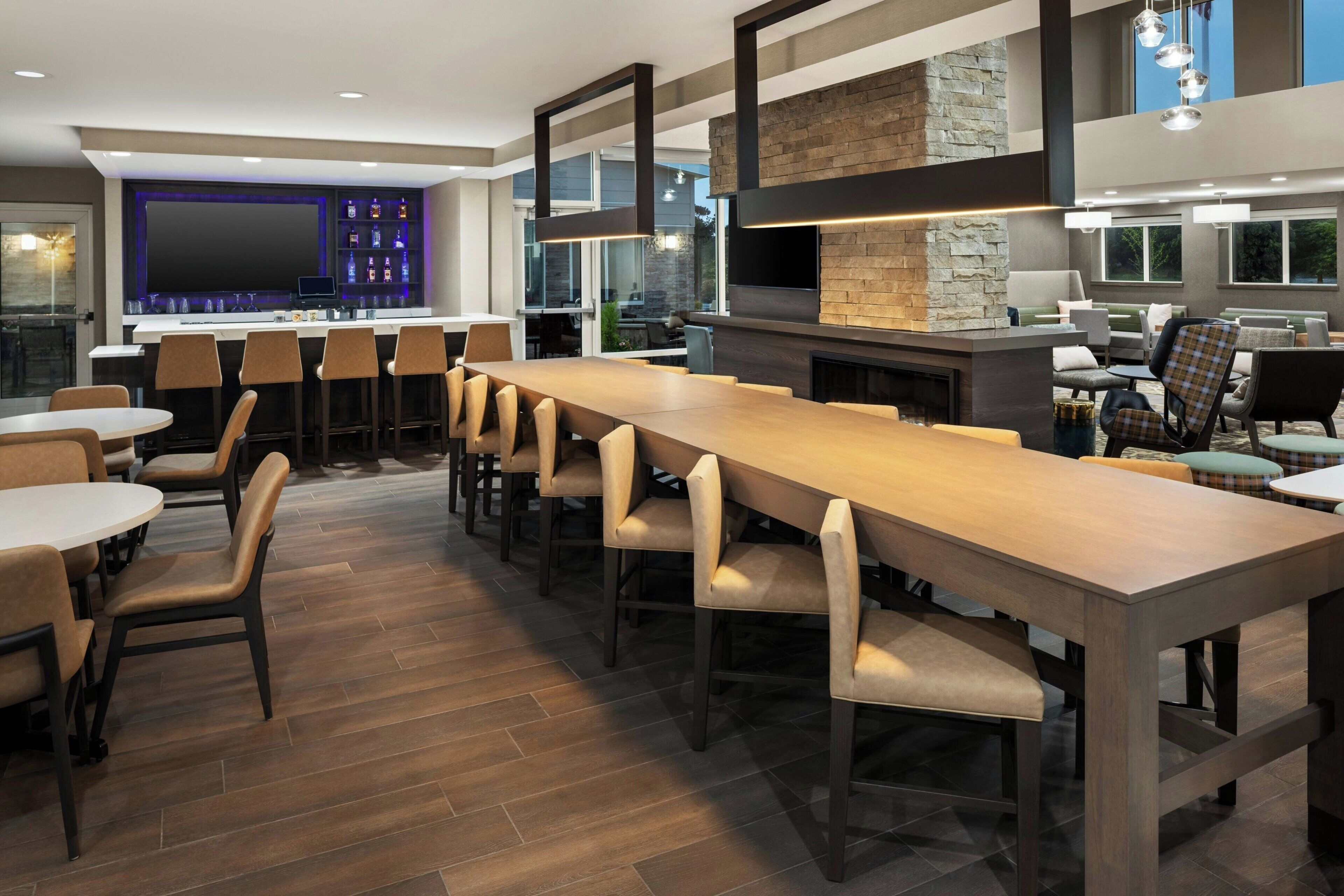 A modern bar area with a long wooden table, multiple bar stools, and a stone accent wall.