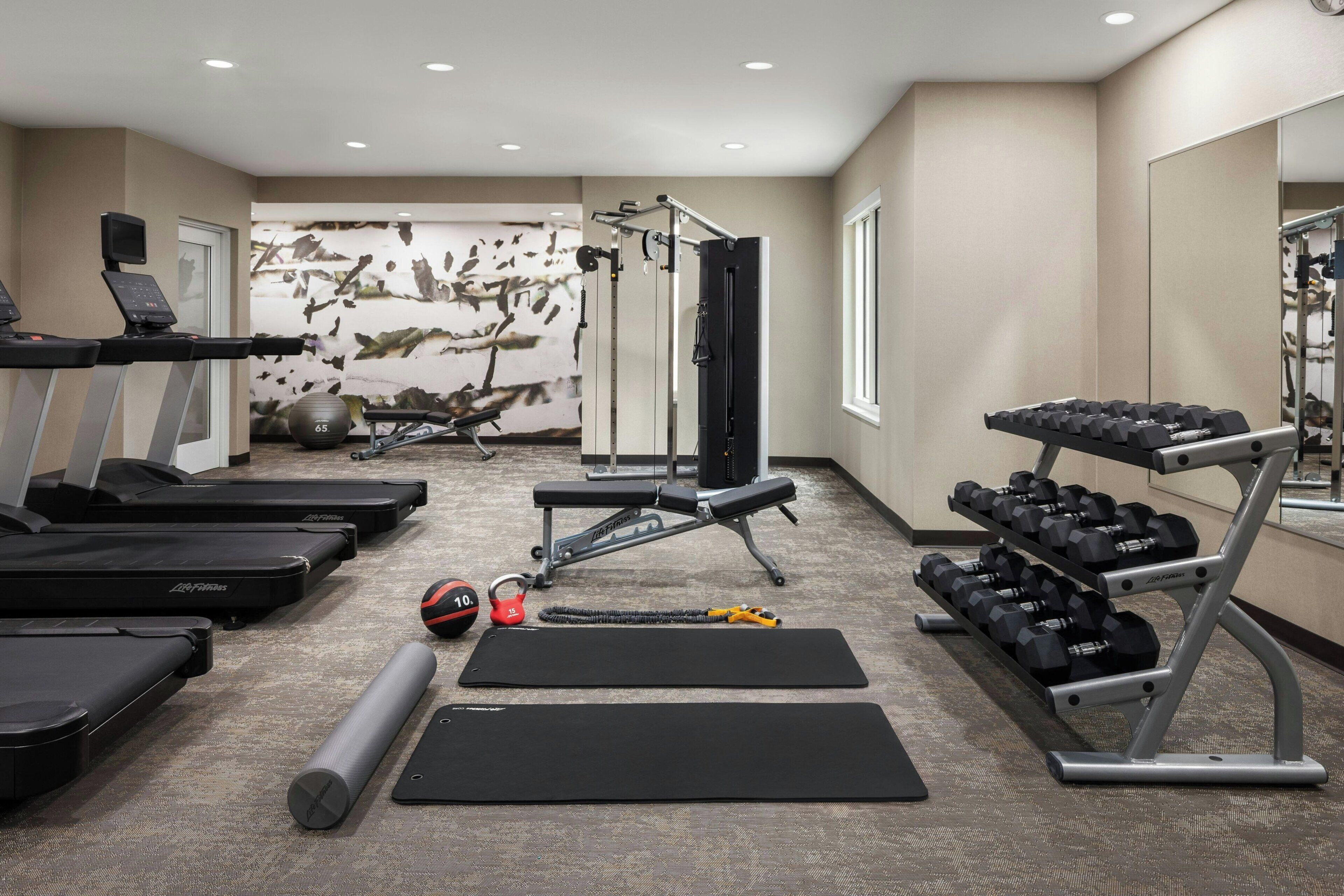 A gym with treadmills, a bench, dumbbells, and exercise balls.