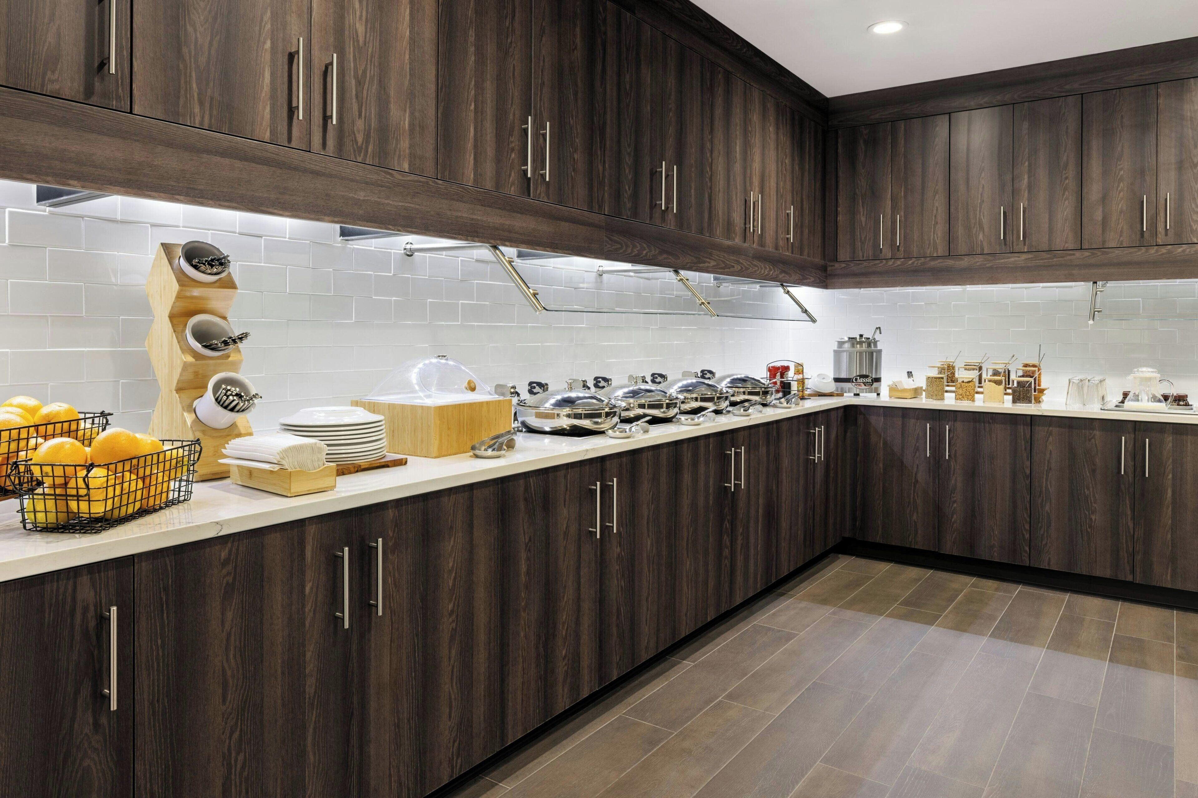 A modern kitchen with dark wood cabinets, white tiled backsplash, and a variety of kitchenware and utensils on the counter.