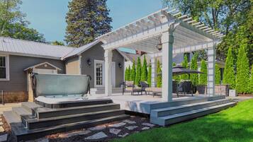 Une terrasse extérieure couverte, dotée d’un jacuzzi, d’un espace salon et d’un escalier menant à la maison.