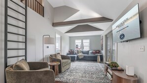A modern living room with a sofa, armchairs, a coffee table, a TV, and a large window.
