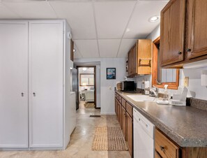 A kitchen with wooden cabinets, a microwave, a dishwasher, and a sink. - Cozy Keaton Cottage | Steps away from Lake MI (Muskegon)
