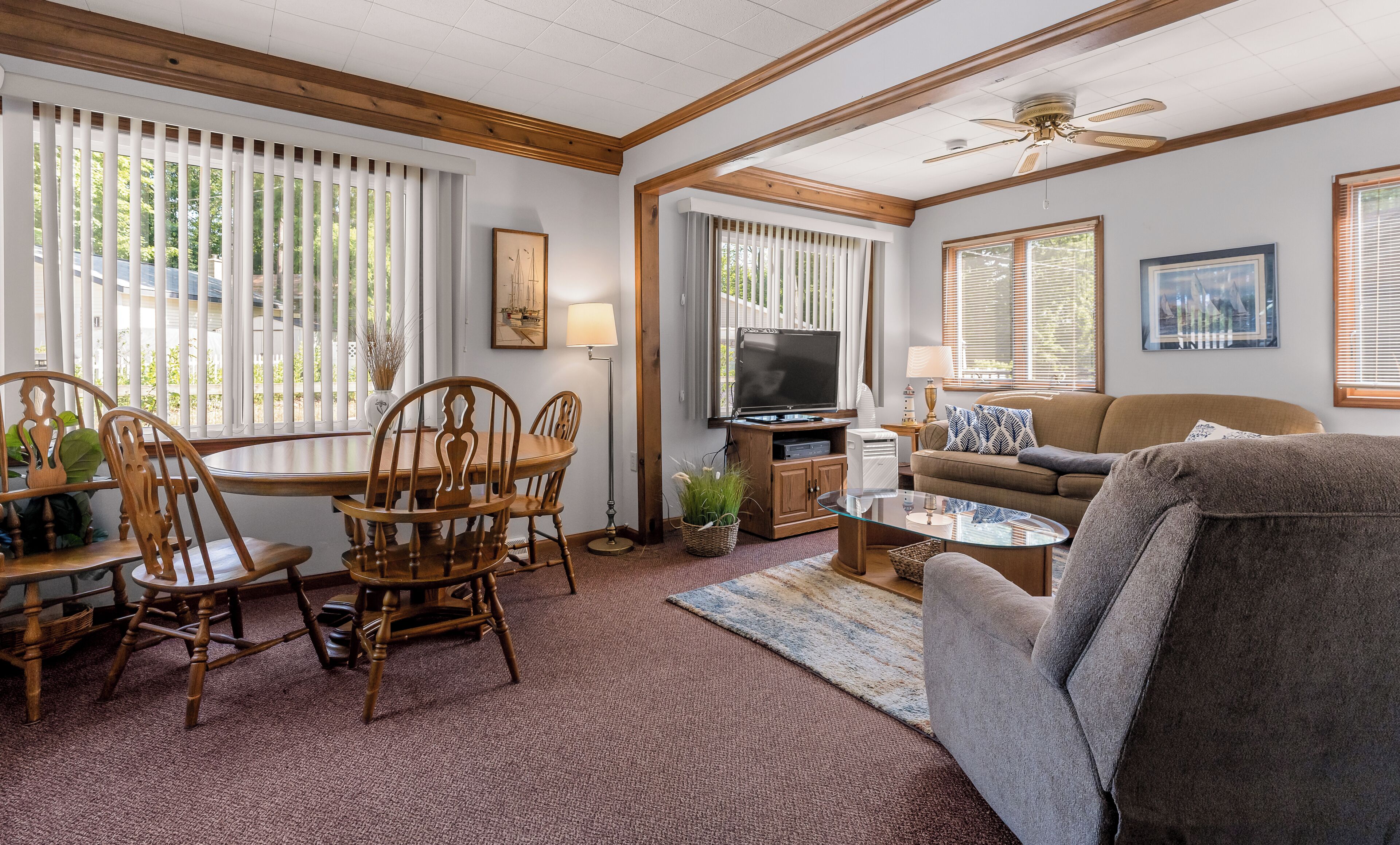 A living room with a television, wooden furniture, and large windows.