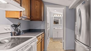 Cocina compacta con armarios de madera, un refrigerador de acero inoxidable, horno integrado y lavadora.