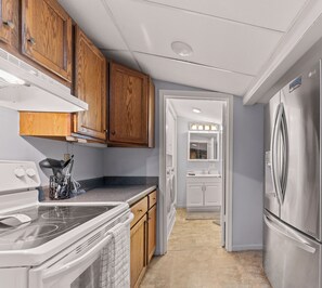 A compact kitchen with wooden cabinets, a stainless steel refrigerator, a built-in oven, and a washing machine. - Cozy Keaton Cottage | Steps away from Lake MI (Muskegon)