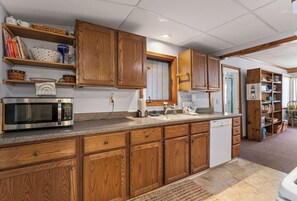 A kitchen with wooden cabinets, a microwave, a dishwasher, and a granite countertop. - Cozy Keaton Cottage | Steps away from Lake MI (Muskegon)