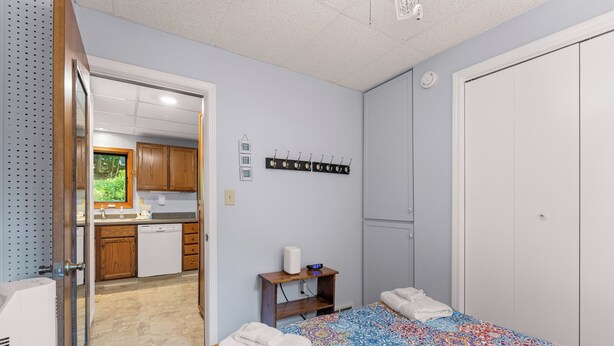 Un dormitorio con cama, mesita de noche, perchero en la pared, armario y vista a la cocina.