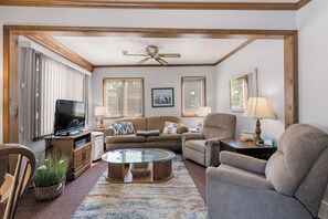 A living room with a television, sofa, armchair, and a ceiling fan. - Cozy Keaton Cottage | Steps away from Lake MI (Muskegon)