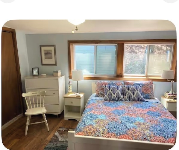 A bedroom with a bed, a chair, a desk, and a window.