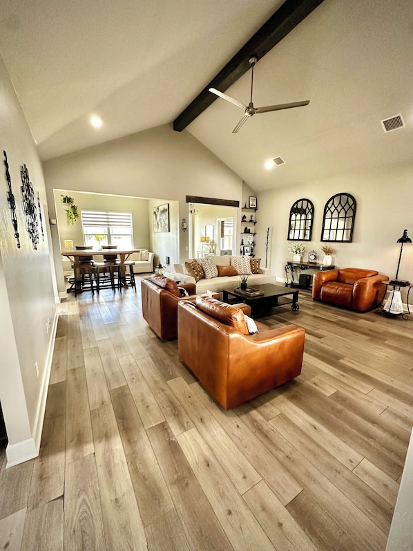 A spacious living room with leather sofas, a dining area, and a ceiling fan.