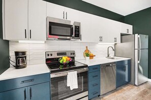 Una cocina moderna con armarios blancos, un microondas de acero inoxidable, un horno empotrado y un lavavajillas.