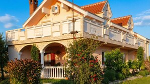 A two-story house with a balcony, a chimney, and a garden with various plants and flowers. - Pool Apartment Rose 1, Privlaka, Croatia (Privlaka)