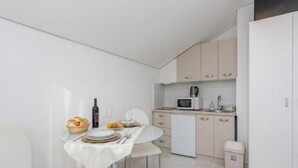 A modern kitchen with a dining area, white cabinetry, a microwave, and a small trash bin. - Pool Apartment Sea 2, Privlaka, Croatia (Privlaka)