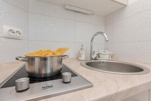 A kitchen with a pot of pasta on an induction cooktop, a sink, and a wall-mounted outlet. - Pool Apartment Lavander 3, Privlaka, Croatia (Privlaka)