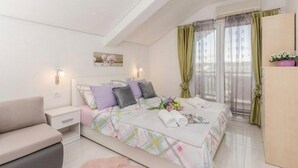 Un dormitorio con cama, mesita de noche, sofá, ventana con cortinas y una pequeña mesa con un jarrón de flores.