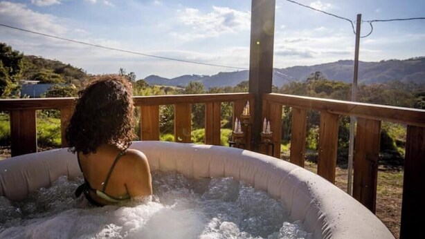 A person in a hot tub with a wooden deck and a scenic view of mountains.