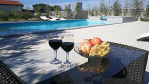 Ein Tisch am Pool mit zwei Gläsern Rotwein, einer Obstschale und Blick auf ein Schwimmbecken.