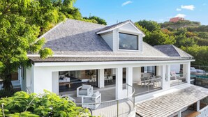 Ein modernes Haus mit überdachter Terrasse, großem Fenster und Blick auf einen Hügel.