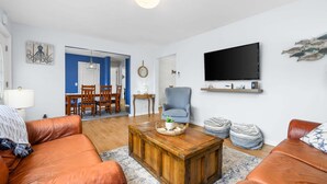 Un salon avec une table basse en bois, des canapés en cuir, un téléviseur et un coin repas comprenant des chaises et une table.