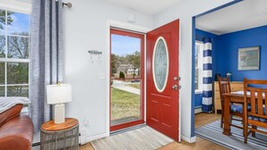 Une pièce avec une porte rouge, un mur blanc, un mur bleu, un plancher en bois, une petite table ronde avec une lampe, une chaise et un tapis.