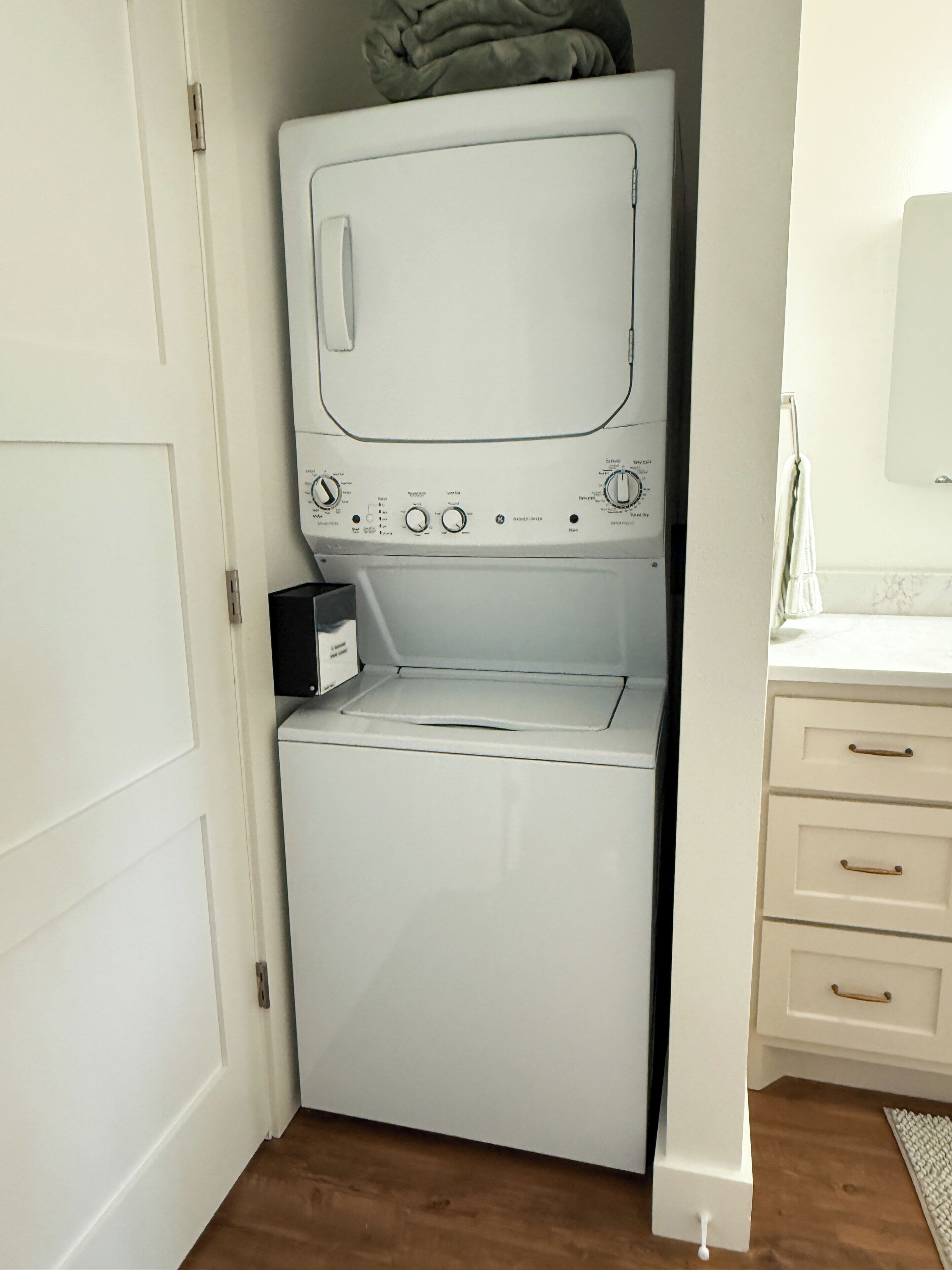 Une petite buanderie comprenant un lave-linge et un sèche-linge, un petit meuble de rangement et un plancher en bois.