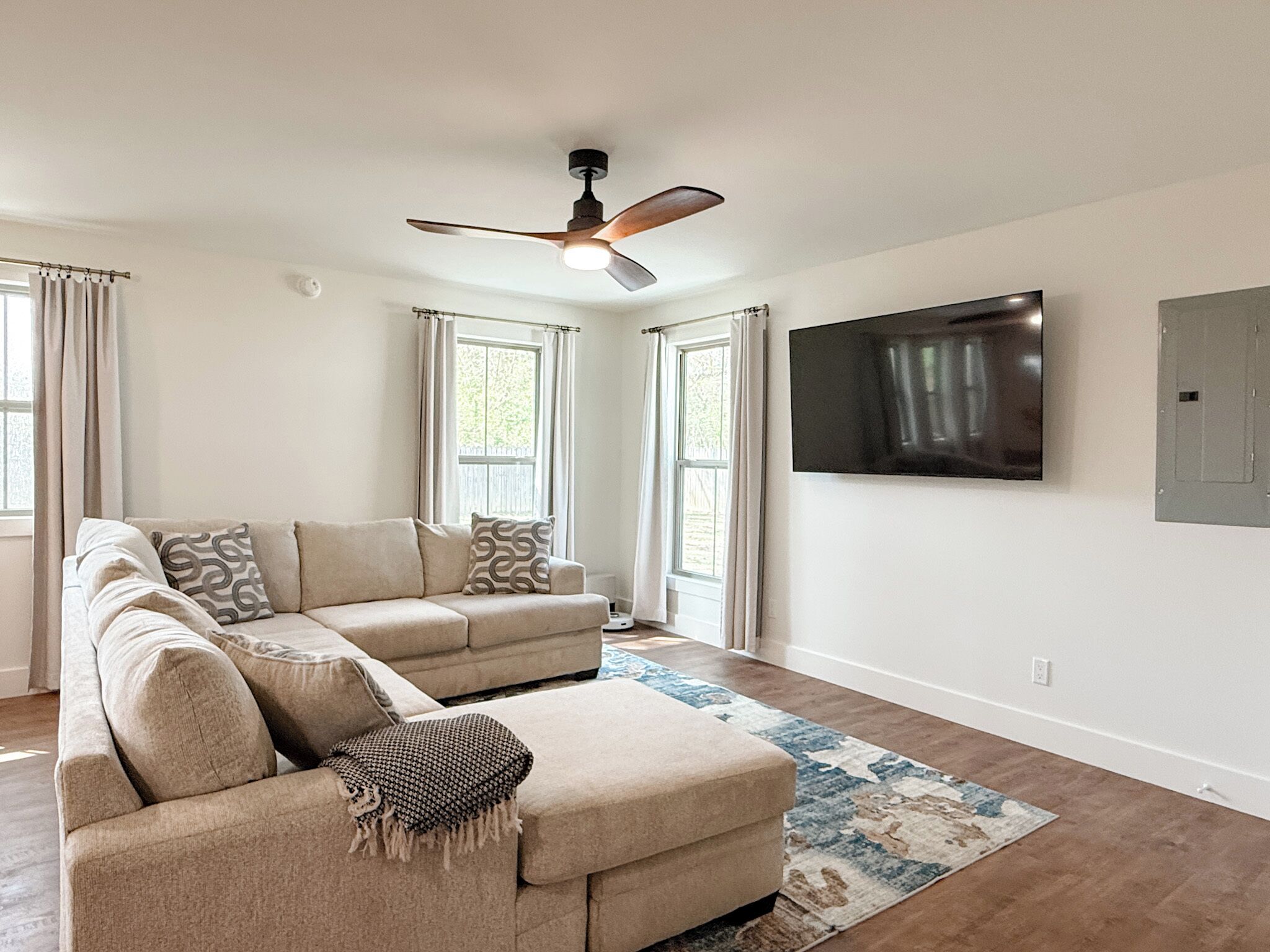 A living room with a sectional sofa, a ceiling fan, a flat-screen TV, and a patterned rug.