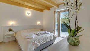 Quarto com cama, mesas de cabeceira, uma orquídea em vaso e vista por uma porta de vidro.