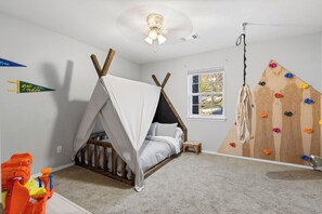 A bedroom with a bed, a climbing wall, a window, and a ceiling fan.