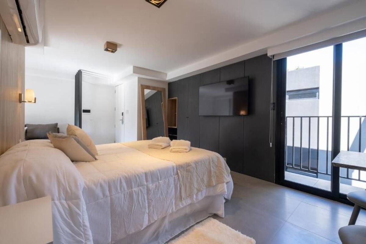 Een moderne hotelkamer met een groot bed, een aan de muur bevestigde televisie en een balkon met een tafel.