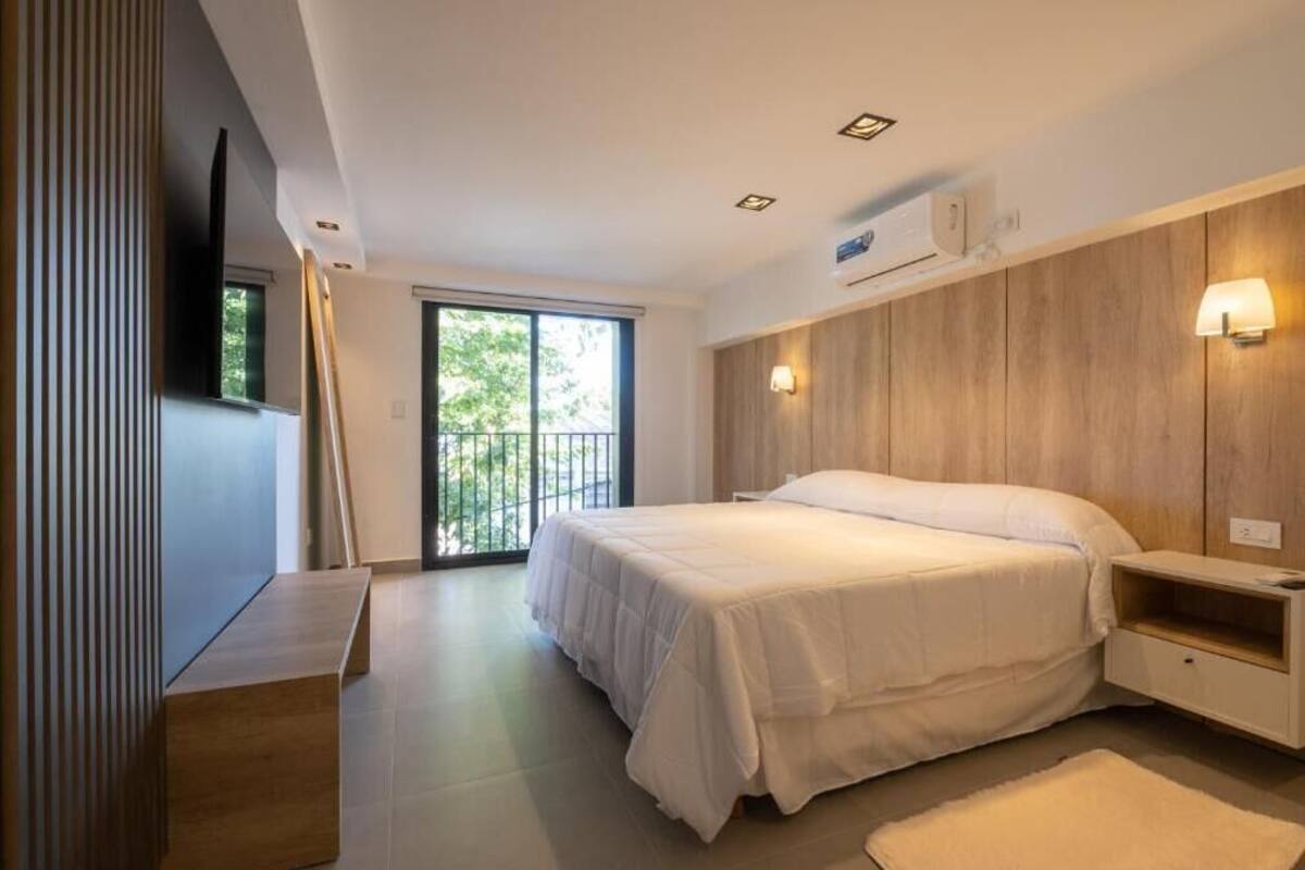 Een moderne slaapkamer met een groot bed, een houten paneelwand, een nachtkastje en een raam met uitzicht.