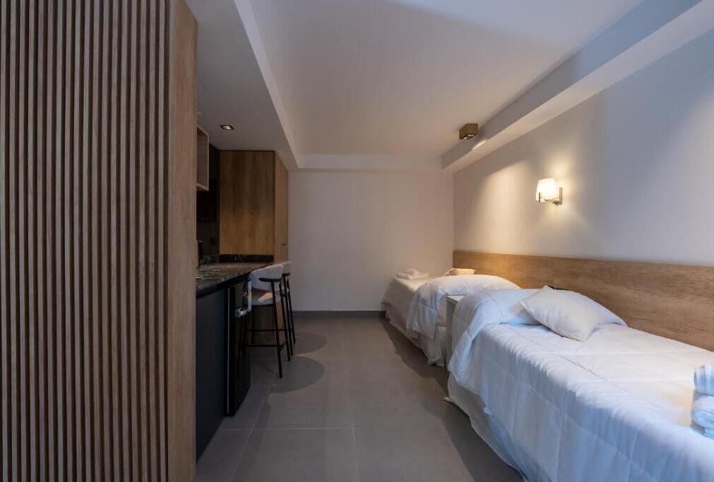 Habitación de hotel con kitchenette, una cama, una mesita de noche y una lámpara de pared.