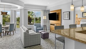 A modern hotel room with a dining area, a sofa, a TV, and a view of the outdoors. - Marriott Desert Springs Villas II near Coachella (Palm Desert)