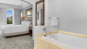 A hotel room with a large bed, a separate bathroom with a bathtub, and a view of the outdoors. - Marriott Desert Springs Villas II near Coachella (Palm Desert)