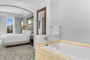 A hotel room with a large bed, a separate bathroom with a bathtub, and a view of the outdoors. - Marriott Desert Springs Villas II near Coachella (Palm Desert)