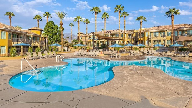 A resort pool area with multiple lounge chairs and umbrellas, surrounded by palm trees and hotel buildings. - Marriott Desert Springs Villas II near Coachella (Palm Desert)