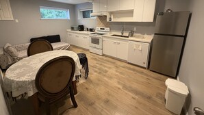 A compact kitchen with white cabinets, a stainless steel refrigerator, a dishwasher, and a dining area with a table and chairs. - Vancouver in Style - Newly listed renovated home in Delta's Sunshine Hills (Delta)