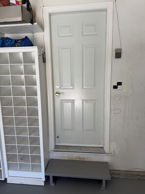A white door with a small step leading up to it, a white metal gate with a grid pattern, and a wall with electrical outlets.