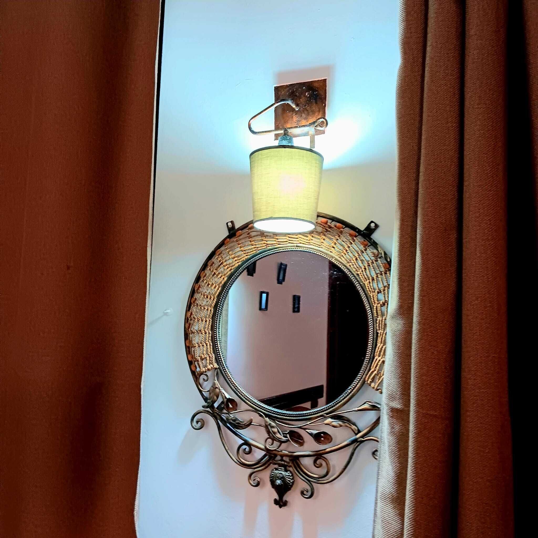 Un miroir fixé au mur, doté d’un cadre orné, un luminaire placé au-dessus et un rideau qui recouvre partiellement le miroir.