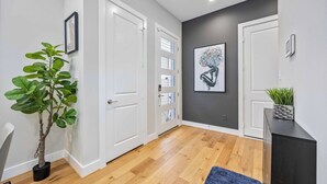 Ein Flur mit Holzboden, weißen Türen, einem Blumentopf und einem gerahmten Kunstwerk an der Wand.