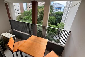 A balcony with a table and chairs, a view of buildings and trees, and a railing. - Dommy (São Paulo)