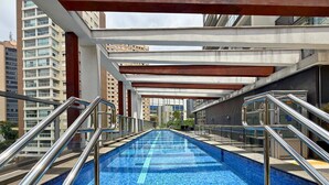 A modern indoor swimming pool with metal railings, surrounded by high-rise buildings. - Dommy (São Paulo)