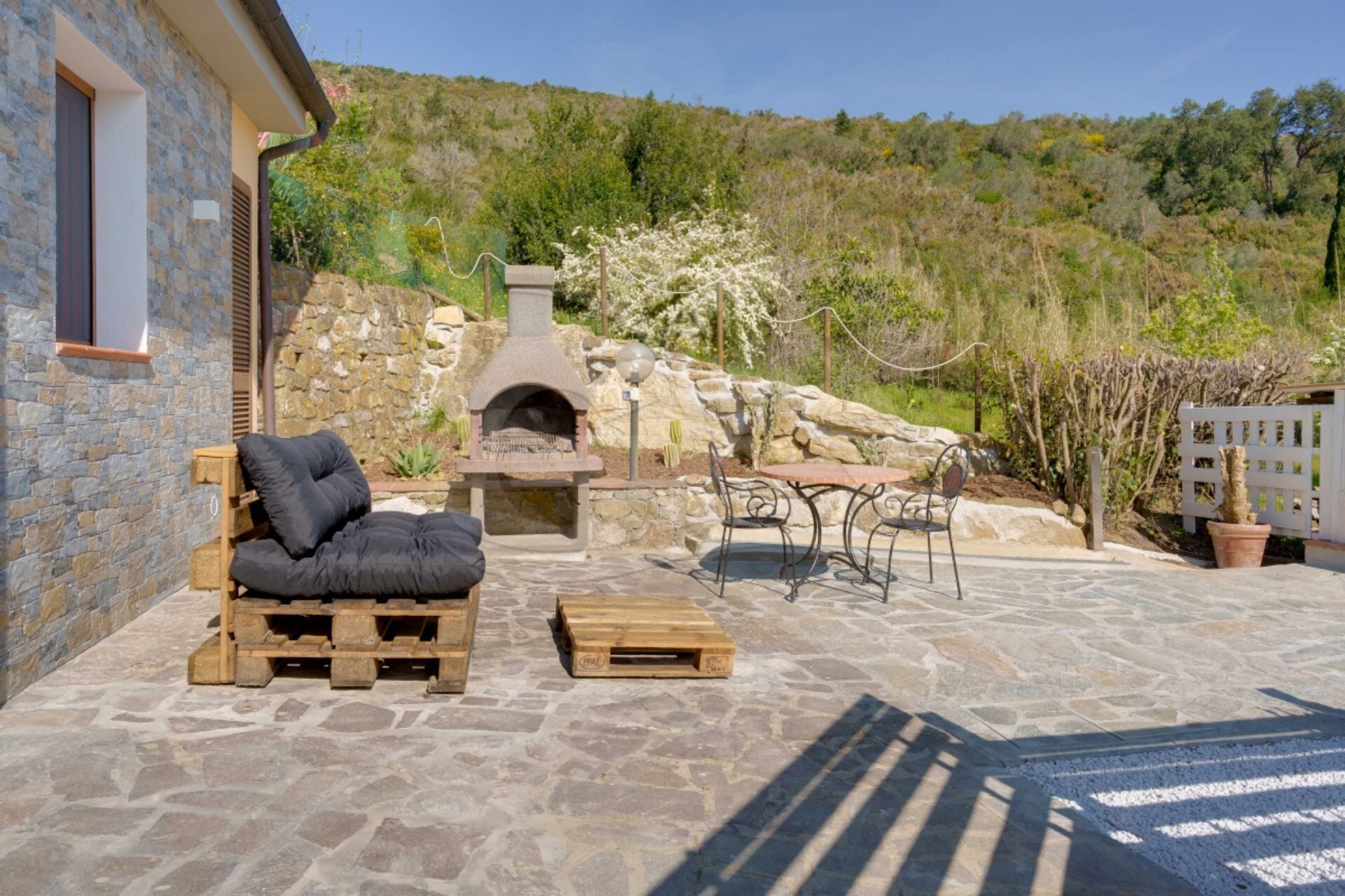 A stone patio with a pizza oven, outdoor seating, and a view of a hillside.
